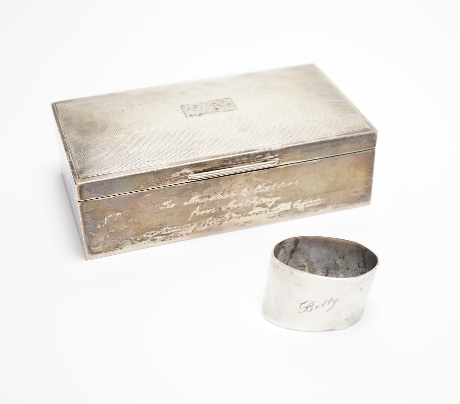 A modern part engine turned silver cigarette box, with engraved inscription, 16cm and a silver serviette ring.